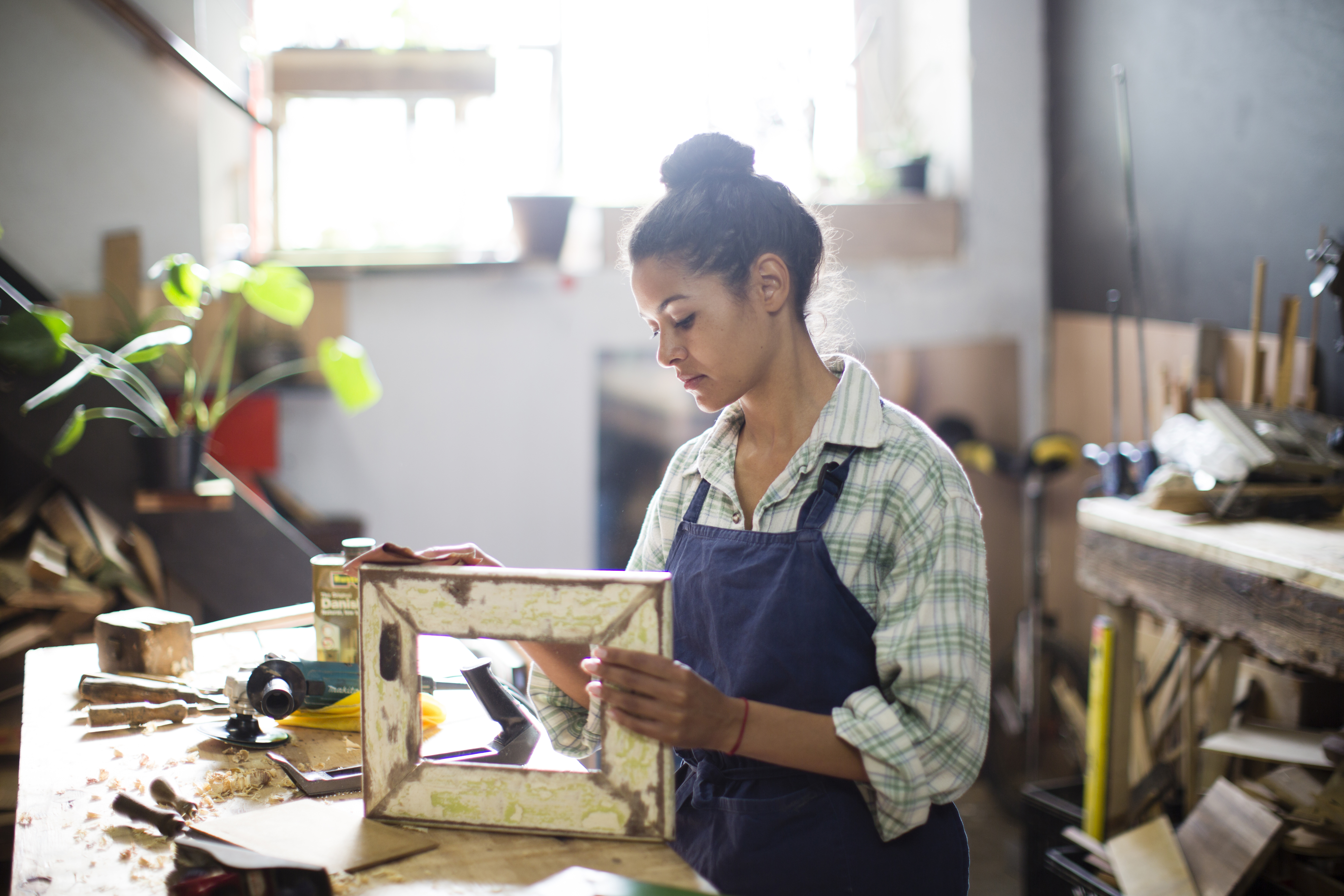 Craftswoman sanding down a recycled wooden picture frame in her workshop